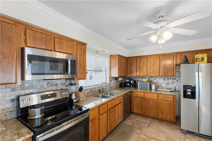 Kitchen featuring sink, backsplash, stainless steel appliances, ornamental molding, and light stone countertops