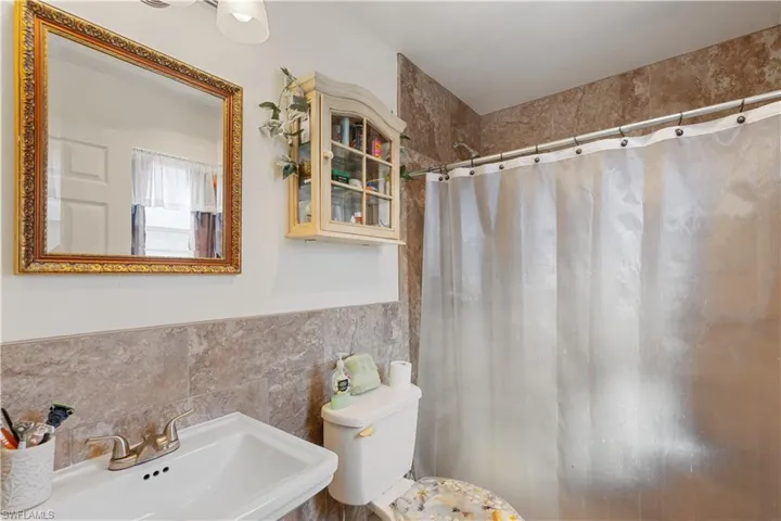Bathroom featuring a shower with curtain, sink, tile walls, and toilet