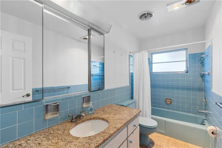 Full bathroom featuring shower / tub combo with curtain, vanity, toilet, and tile walls