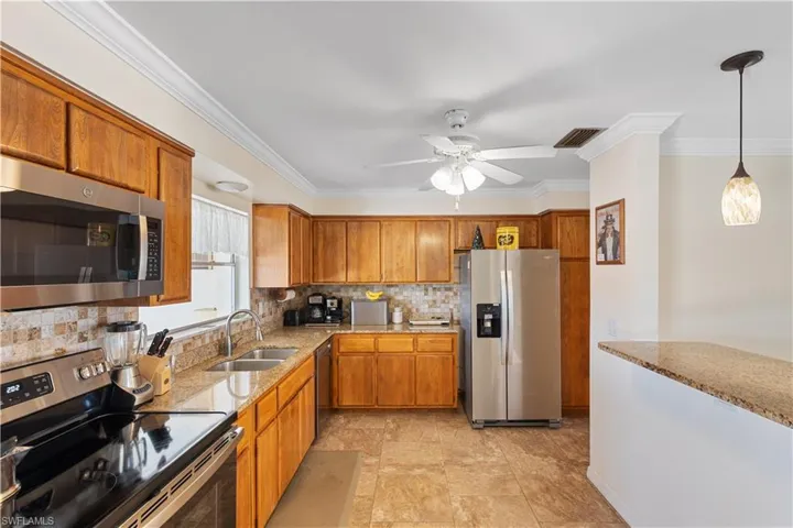 Kitchen featuring appliances with stainless steel finishes, pendant lighting, sink, decorative backsplash, and crown molding