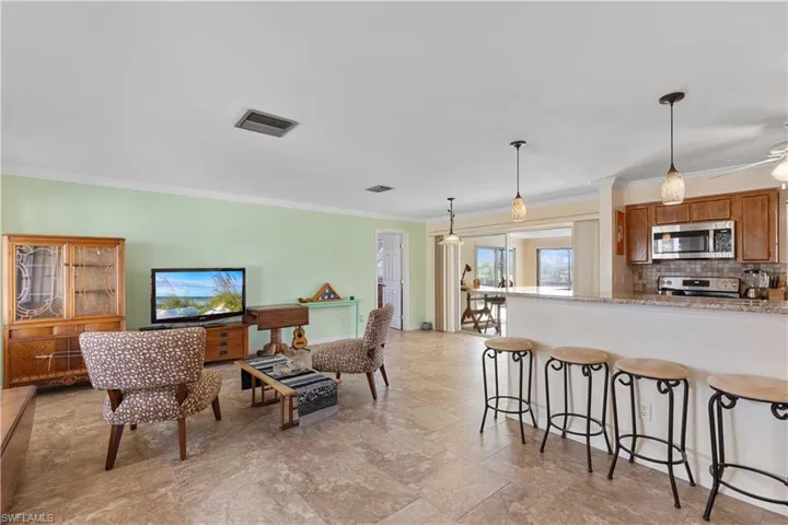 Kitchen featuring light stone counters, hanging light fixtures, ornamental molding, stainless steel appliances, and backsplash
