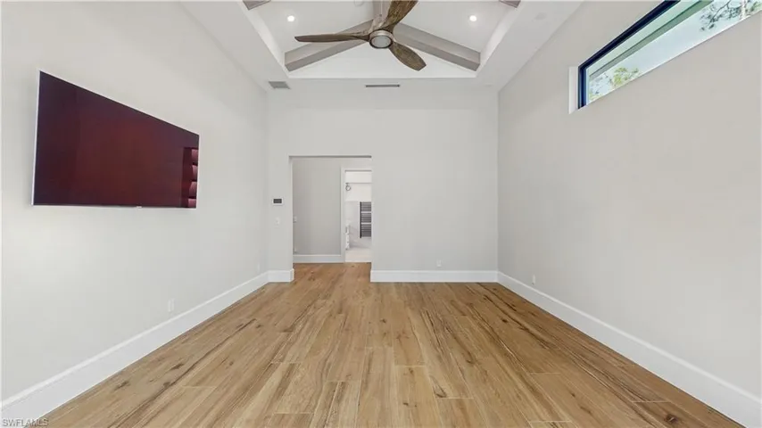 Spare room featuring a towering ceiling, ceiling fan, beam ceiling, and light hardwood / wood-style flooring