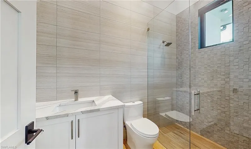 Bathroom with toilet, a shower with door, vanity, and tile walls