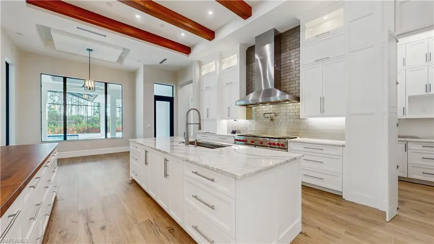 Kitchen with stainless steel range, white cabinets, a kitchen island with sink, and wall chimney range hood