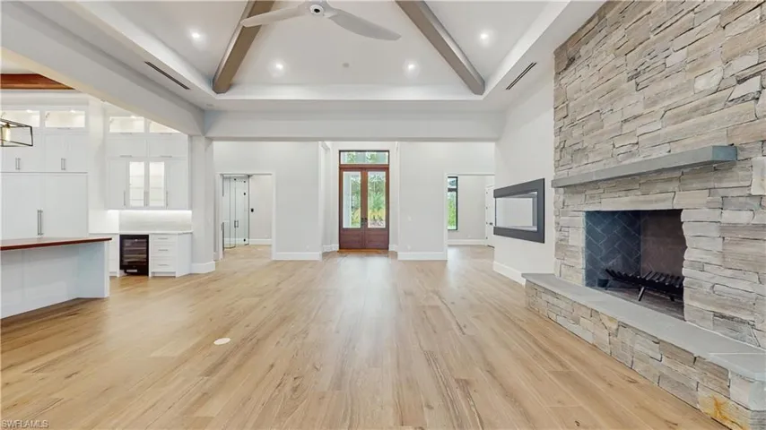 Unfurnished living room featuring beamed ceiling, ceiling fan, light hardwood / wood-style flooring, wine cooler, and a stone fireplace