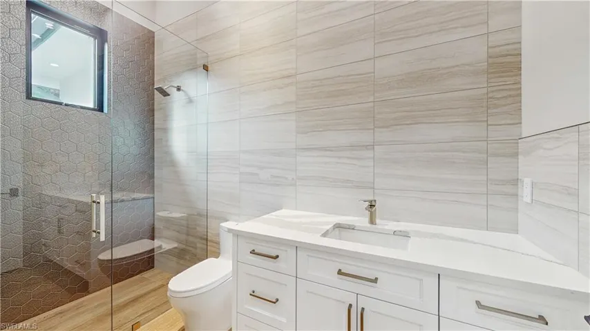 Bathroom with toilet, an enclosed shower, vanity, and tile walls