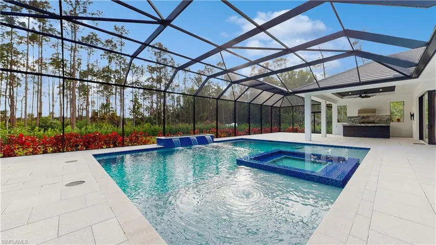 View of pool with an in ground hot tub, a patio, an outdoor kitchen, glass enclosure, and pool water feature