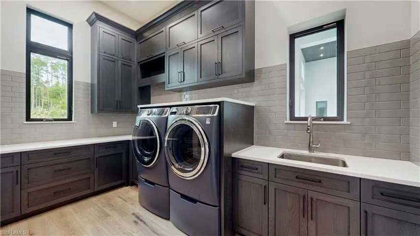 Clothes washing area featuring sink, washer and dryer, cabinets, and light hardwood / wood-style flooring
