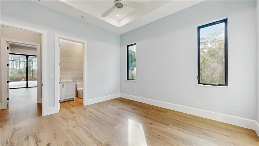 Unfurnished bedroom with ensuite bath, ceiling fan, light hardwood / wood-style floors, and multiple windows