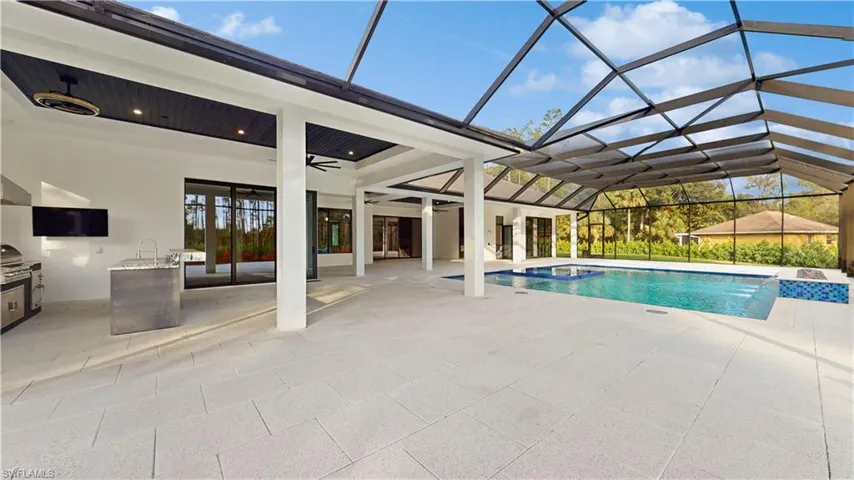 View of pool with a patio area, an outdoor kitchen, glass enclosure, ceiling fan, and pool water feature