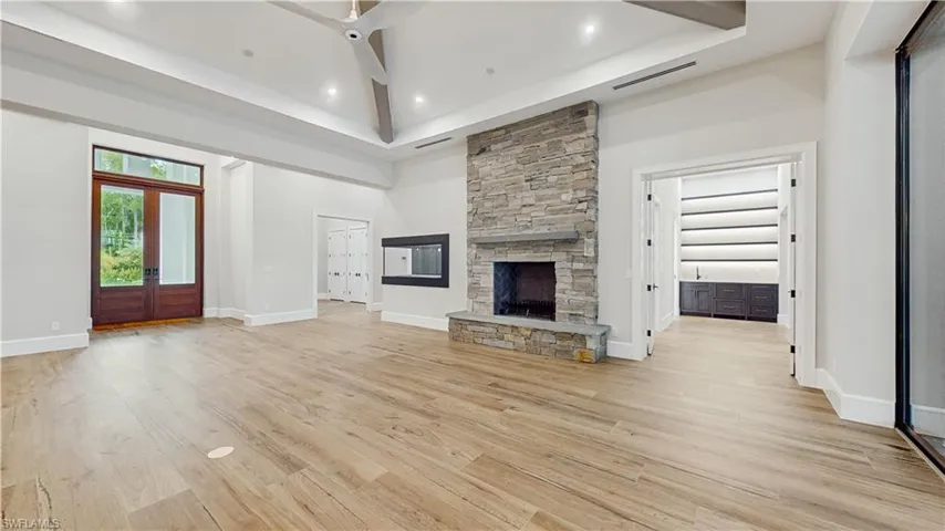 Unfurnished living room with a fireplace, french doors, ceiling fan, light wood-type flooring, and a high ceiling