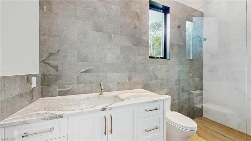 Bathroom featuring toilet, a tile shower, vanity, and tile walls