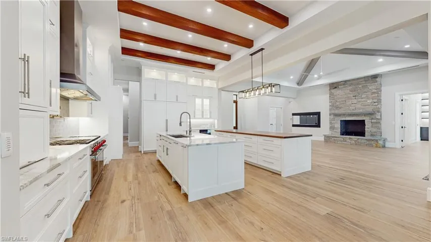 Kitchen with white cabinets, a stone fireplace, wall chimney exhaust hood, and a center island with sink