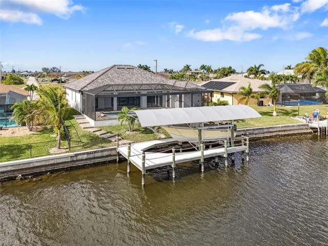Dock area with glass enclosure, boat lift, a yard, and a water view