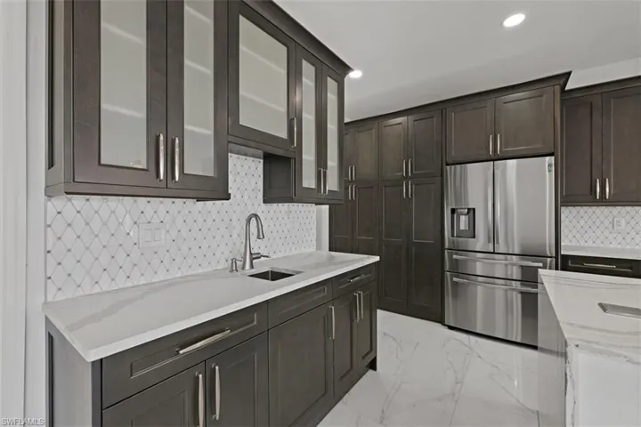 Kitchen featuring stainless steel refrigerator with ice dispenser, light stone counters, decorative backsplash, light marble finish flooring, and dark brown cabinetry
