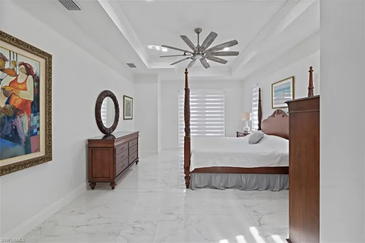 Bedroom featuring crown molding, a ceiling fan, light marble finish flooring, and a raised ceiling