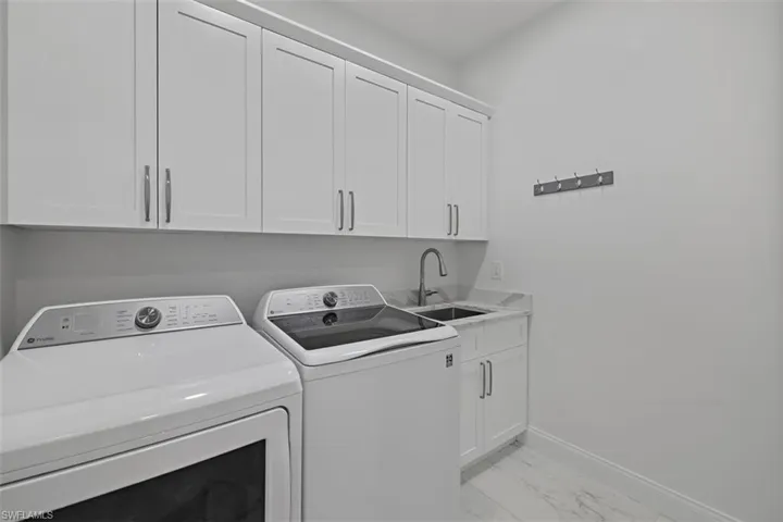 Laundry area with light marble finish floors, washing machine and clothes dryer, and cabinet space