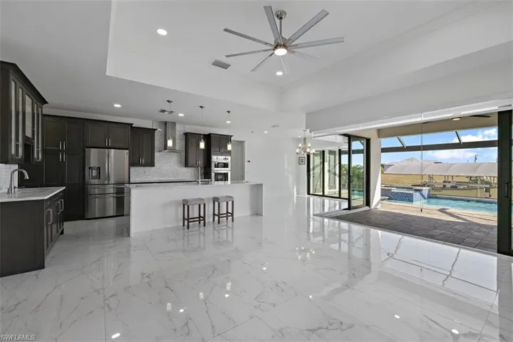 Kitchen featuring open floor plan, stainless steel appliances, wall chimney exhaust hood, a breakfast bar area, and tasteful backsplash