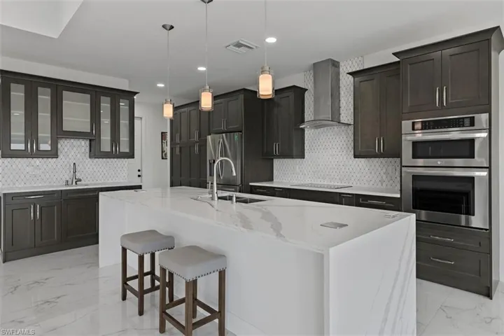 Kitchen featuring light marble finish floors, tasteful backsplash, stainless steel appliances, wall chimney range hood, and a breakfast bar area