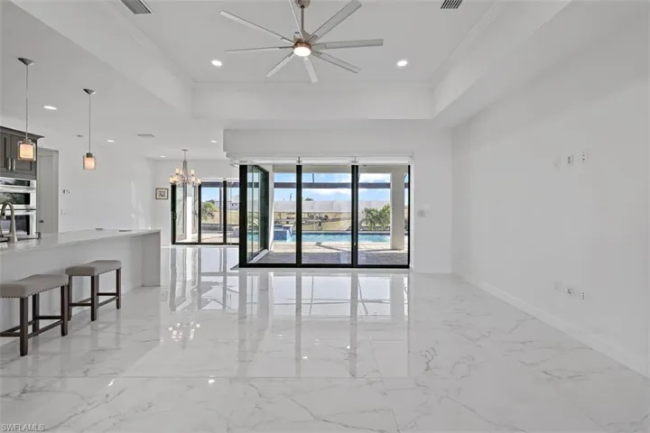 Unfurnished room featuring ornamental molding, a chandelier, a raised ceiling, light marble finish flooring, and recessed lighting