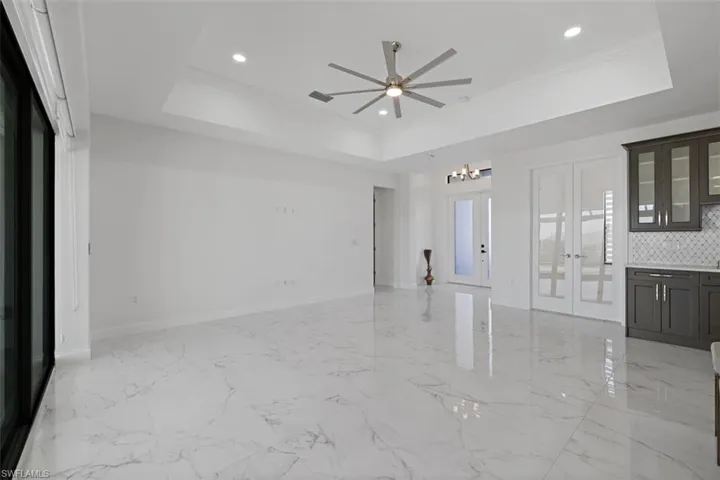 Unfurnished living room with french doors, a chandelier, ornamental molding, recessed lighting, and light marble finish flooring