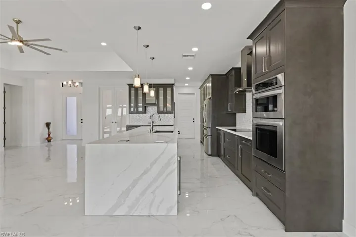 Kitchen with glass insert cabinets, recessed lighting, light stone counters, pendant lighting, and a center island with sink