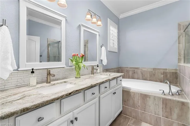 Bathroom with crown molding, double vanity, a bath, and a tile shower