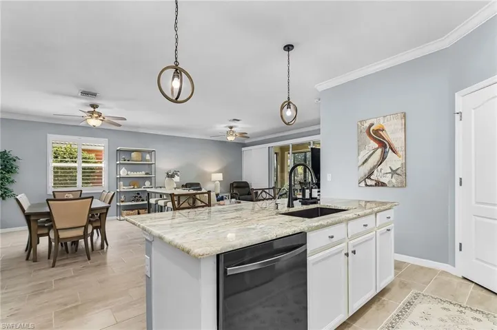 Kitchen with ornamental molding, stainless steel dishwasher, light stone countertops, white cabinets, and an island with sink