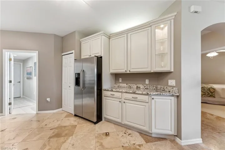 Kitchen featuring glass insert cabinets, arched walkways, white cabinets, and stainless steel fridge