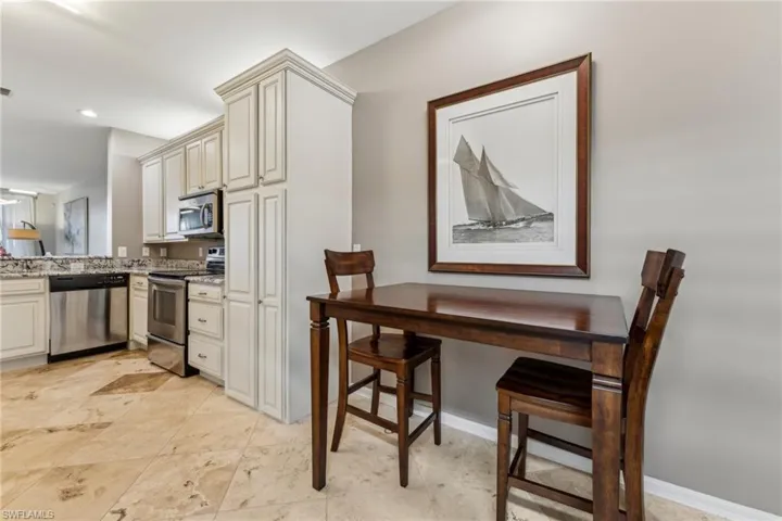 Kitchen featuring light stone countertops, baseboards, stainless steel appliances, and cream cabinetry