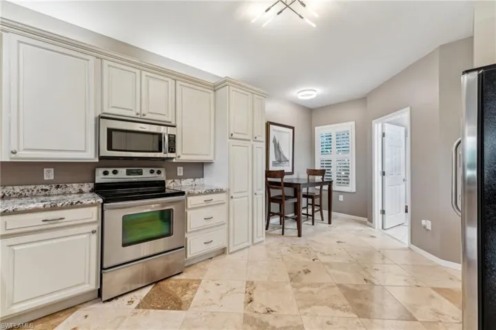 Kitchen featuring light stone countertops, baseboards, appliances with stainless steel finishes, and cream cabinetry