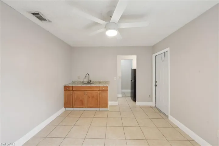 Bar featuring ceiling fan, black fridge, light tile patterned floors, and sink
