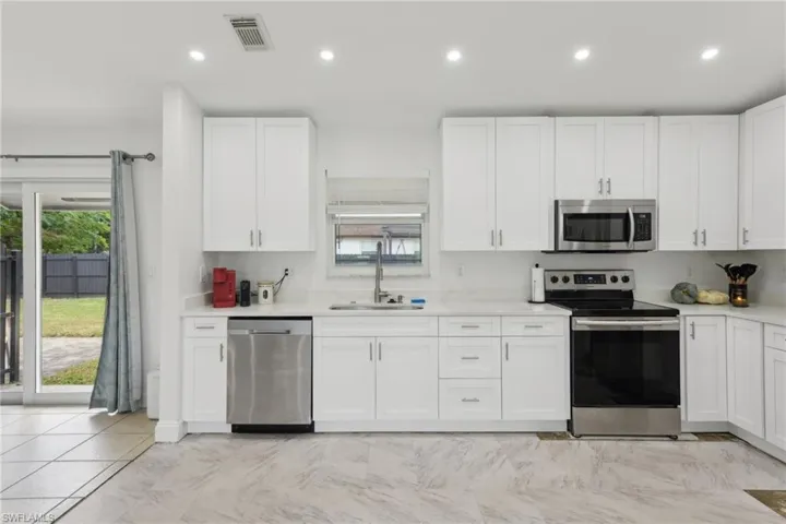 Kitchen with sink, white cabinets, light tile patterned floors, and appliances with stainless steel finishes