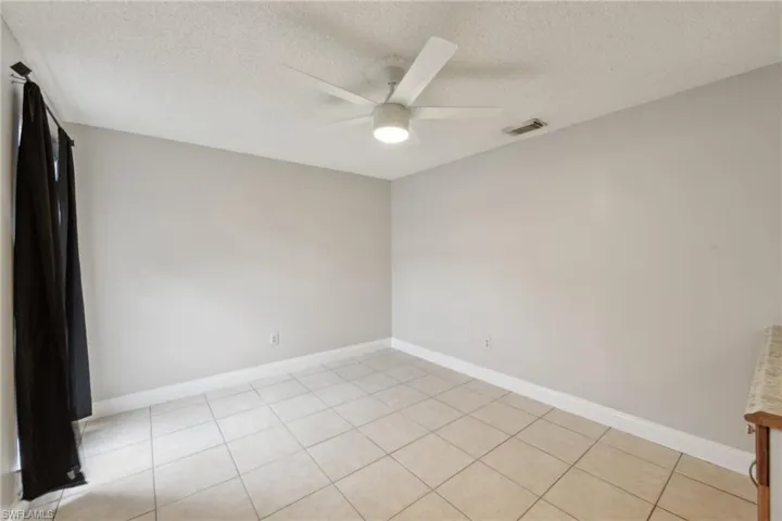 Tiled empty room with ceiling fan and a textured ceiling