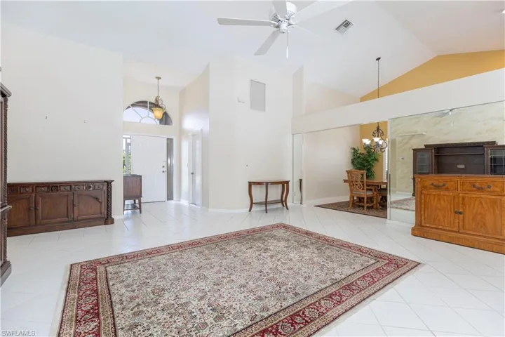 Living room with high vaulted ceiling, ceiling fan with notable chandelier, and light tile floors