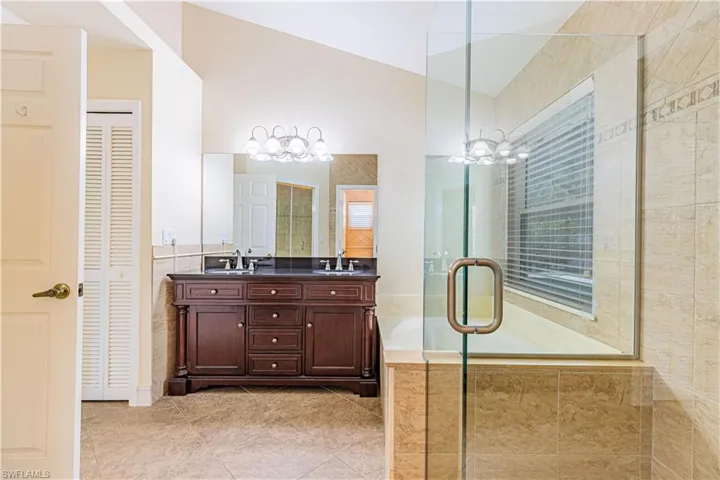 Bathroom featuring a notable chandelier, dual vanity, tile floors, and a shower with door