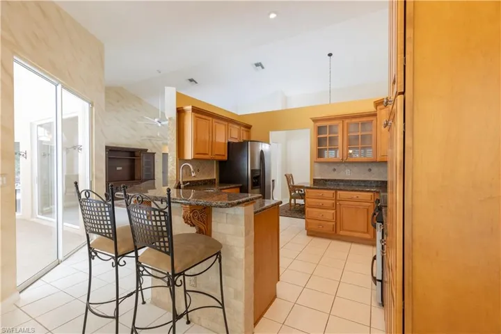 Kitchen with tasteful backsplash, dark stone countertops, light tile floors, a breakfast bar, and stainless steel fridge with ice dispenser