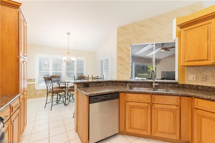 Kitchen with dishwasher, vaulted ceiling, sink, and ceiling fan with notable chandelier