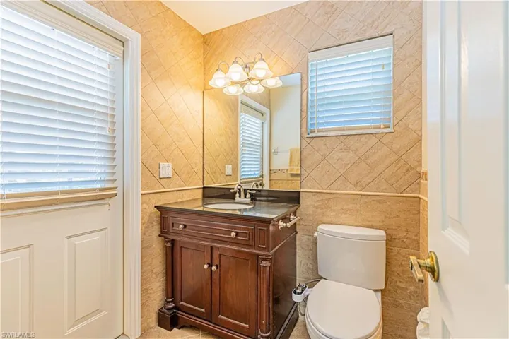 Bathroom with tile flooring, tile walls, toilet, and vanity