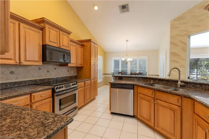 Kitchen featuring decorative light fixtures, dark stone counters, light tile flooring, appliances with stainless steel finishes, and sink