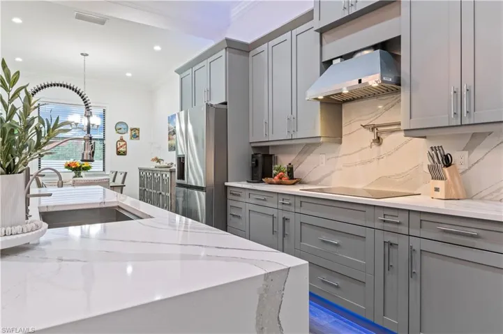 Kitchen with ventilation hood, stainless steel fridge with ice dispenser, gray cabinetry, crown molding, and black electric cooktop
