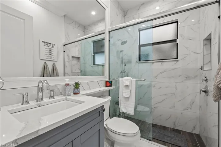 Full bath featuring a marble finish shower, toilet, and vanity