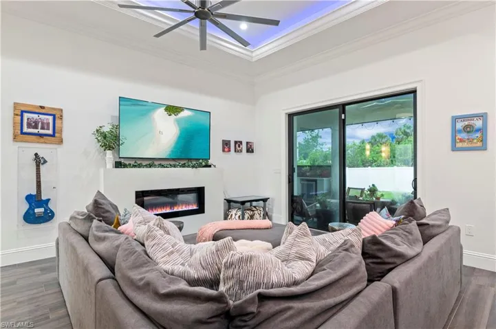 Living room with a glass covered fireplace, dark wood-type flooring, crown molding, and ceiling fan