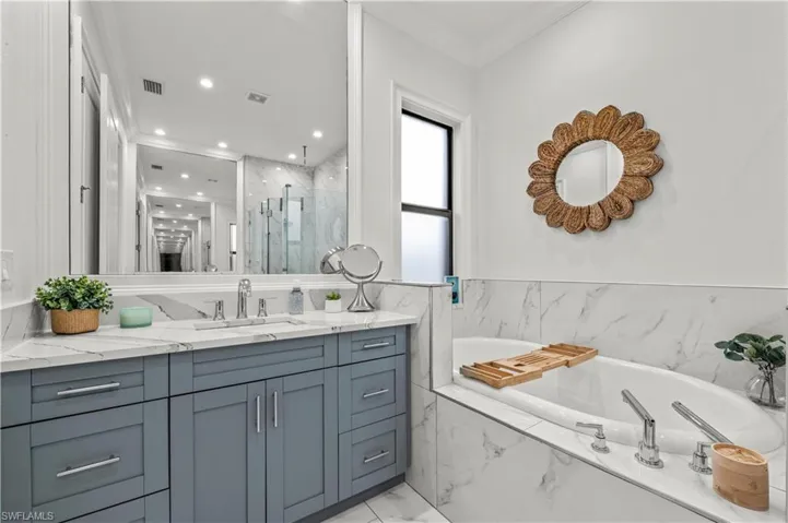 Bathroom featuring visible vents, a garden tub, marble finish floor, a marble finish shower, and vanity