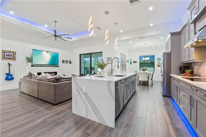 Kitchen with dark wood-style floors, light stone countertops, a sink, stainless steel appliances, and gray cabinetry