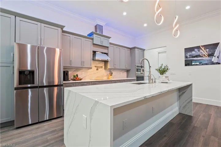 Kitchen with a center island with sink, range hood, stainless steel fridge with ice dispenser, and ornamental molding