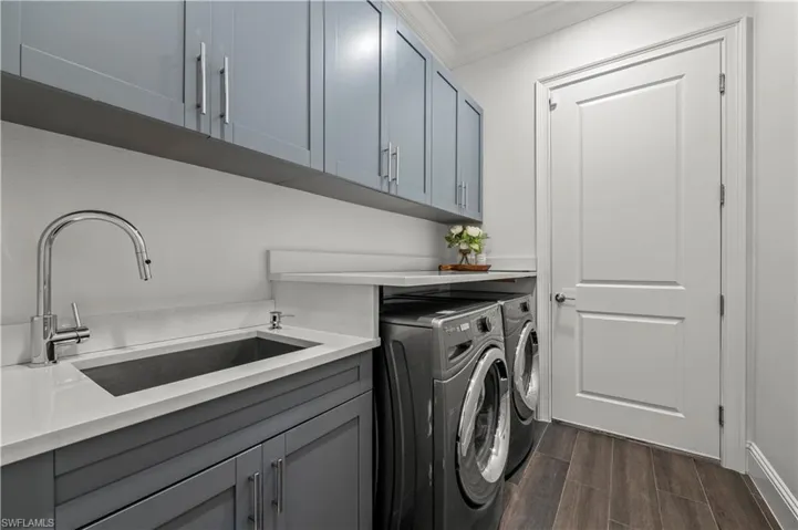Laundry area with wood tiled floor, cabinet space, a sink, ornamental molding, and washer and clothes dryer