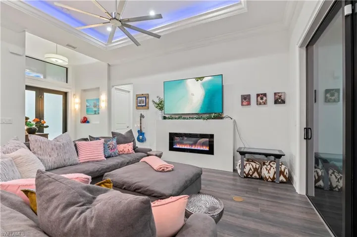 Living area with visible vents, ornamental molding, a tray ceiling, a glass covered fireplace, and dark wood-style flooring