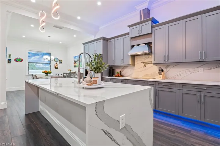 Kitchen with tasteful backsplash, gray cabinetry, crown molding, and extractor fan