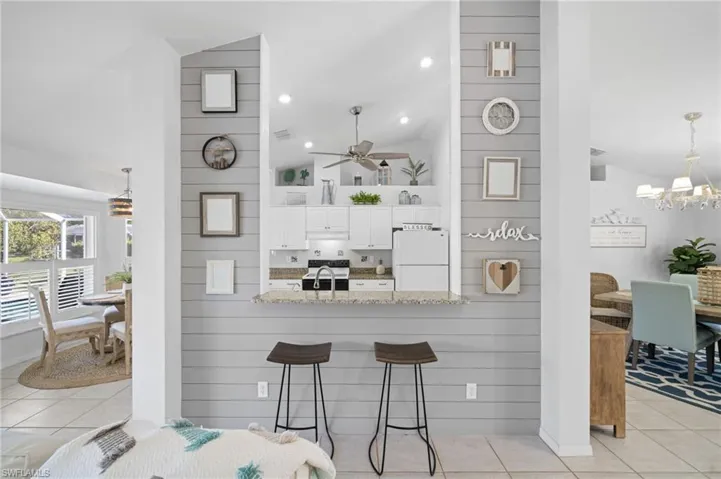 Kitchen featuring white cabinetry, light stone counters, white appliances, a breakfast bar area, and light tile patterned flooring